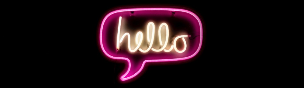 A neon sign with a pink speech bubble. Inside the bubble it says 'hello' in white neon. Photo by Drew Beamer on Unsplash.