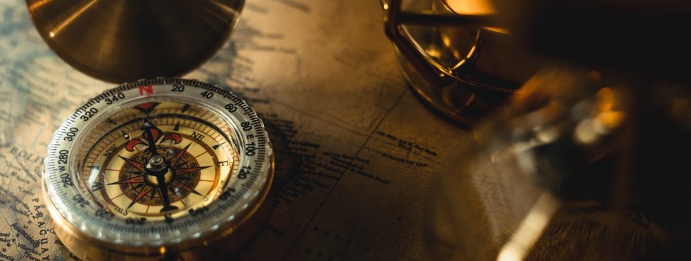 A photo of an old fashioned compass with a blurred map in the background. Photo by Dunamis Church on Unsplash.